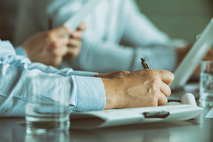 man holding pen and writing in a meeting